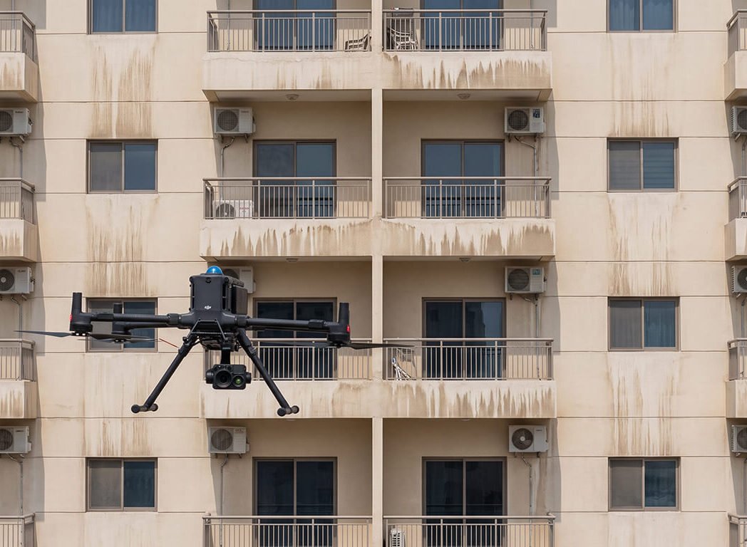 Drone scanning the grid-like facade of a balconied apartment building during a facade inspection