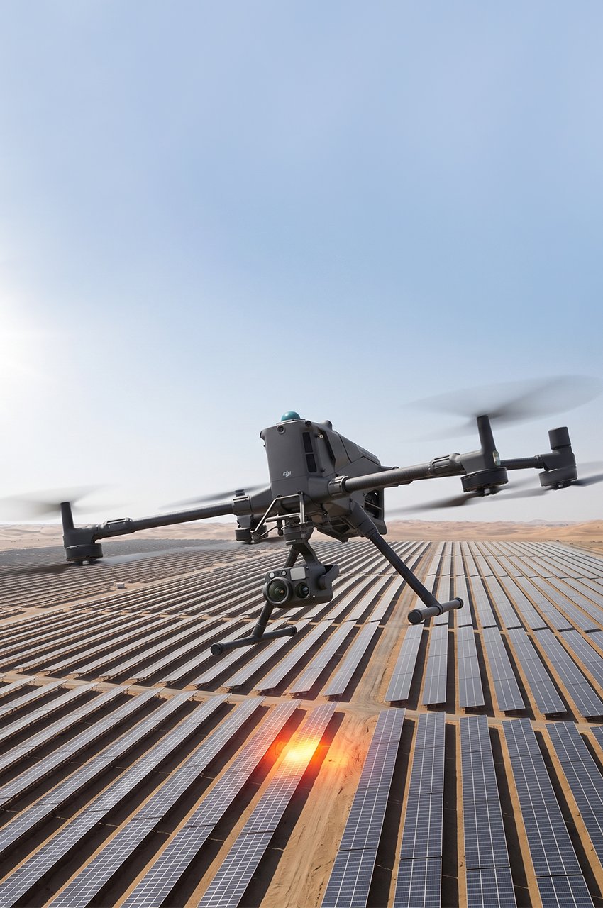 This image shows a DJI Matrice 350 RTK enterprise drone conducting a thermal inspection over a utility-scale solar farm in a desert environment.